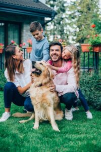 Shot of an adorable young family with two child and cute Golden Retriever posing in backyard of their house.